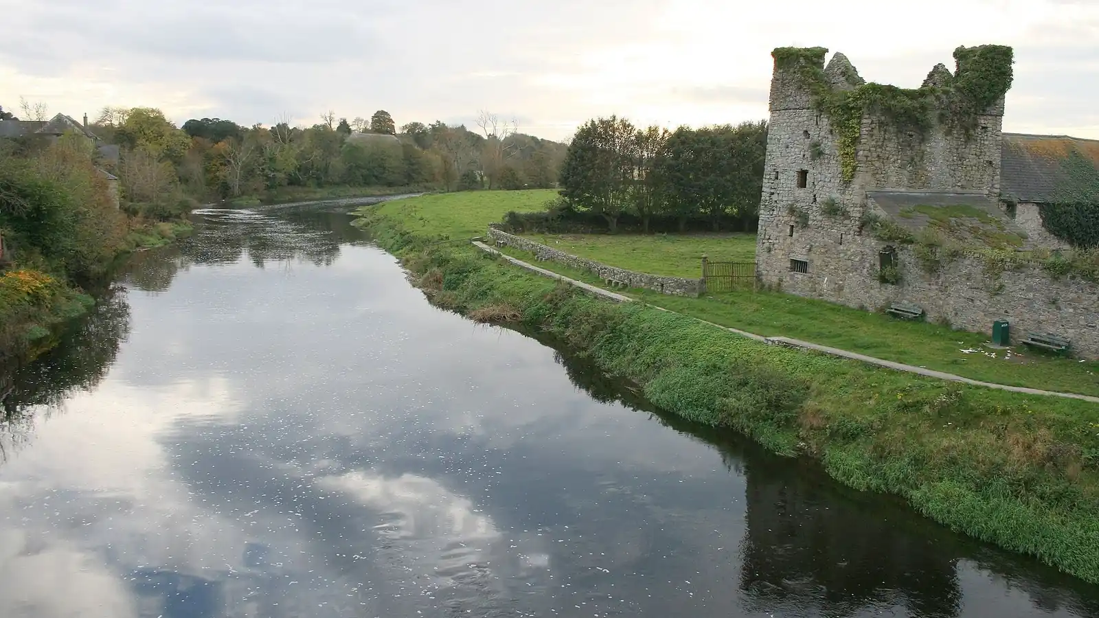 The River Nore at Thomastown, flowing past grassy banks and a ruined stone tower, seen from the bridge.