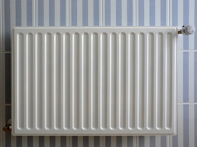 A white panel radiator on a wall tiled in blue and white stripes, with its thermostatic valve at the top right