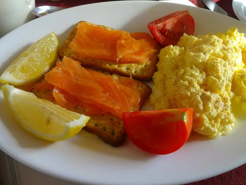 A plate of scrambled eggs with smoked salmon on toasted bread, tomato and lemon wedges.
