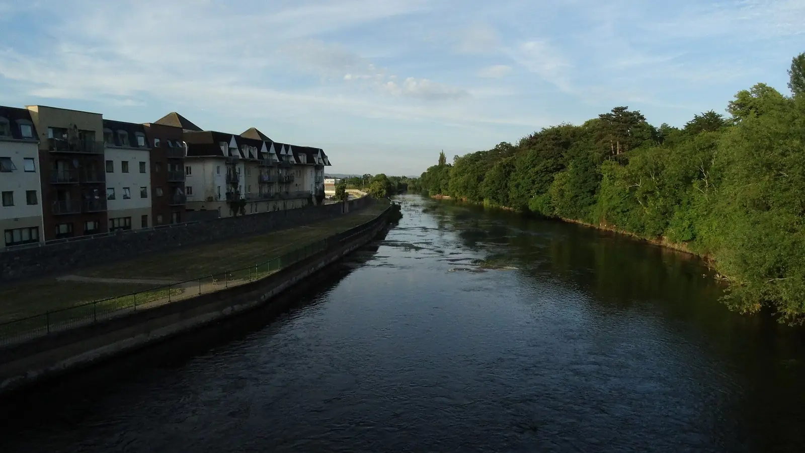 The River Suir running straight through Clonmel at evening, apartments on the left bank and trees on the right.