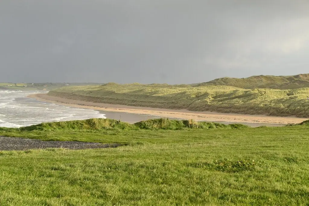 The long sweep of Tullan Strand at low tide, backed by grassy dunes under a heavy sky.