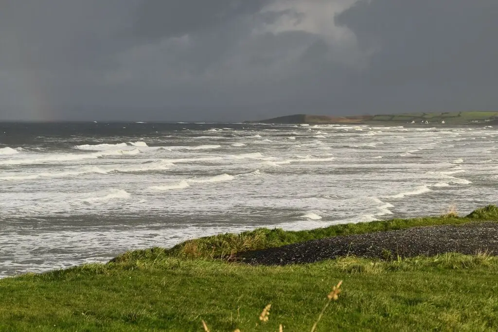 A dark rain squall over rough, white-capped water off Tullan Strand, with a green headland in the distance.